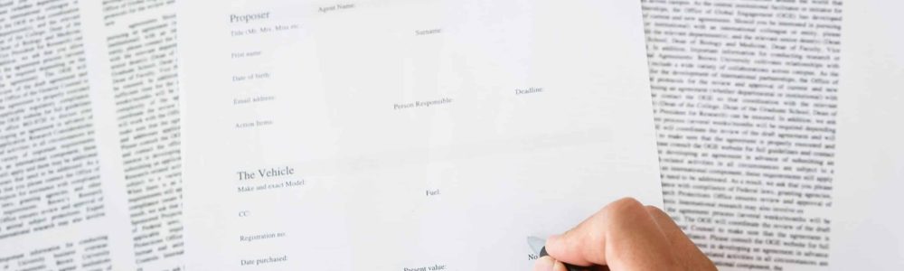 close up of man hands signing a insurance policy form about vehicle.